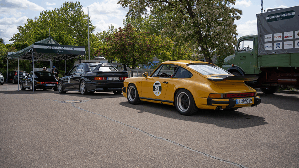 Autos, darunter ein gelber Porsche und ein schwarzer Mercedes, am Start der Oldtimer Rallye Oberschwaben Classic.